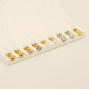 Set of gold ball, zircon, and pearl stud earrings displayed on a white plaster stand