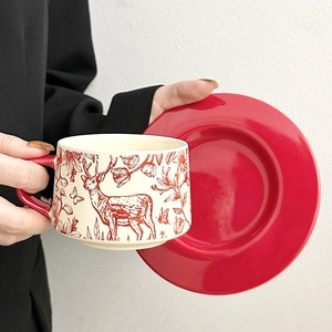 Vintage beige ceramic coffee cup with red deer pattern and matching saucer in hand
