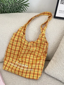 Minimalist orange plaid canvas tote bag with embroidered text on a soft white sofa