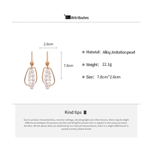 Detail view of gold alloy geometric earrings with white pearls and size 7.8cm x 2.6cm