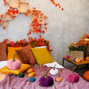 Assorted colorful velvet decorative pumpkins with maple leaves on bed background