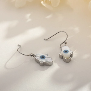 Detailed macro view of silver Hamsa Hand earrings with blue Evil Eye and white shell inlay