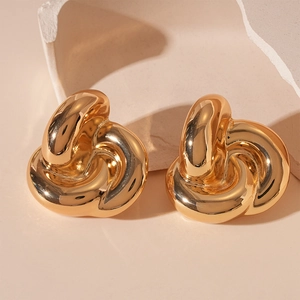 Macro shot of chunky gold knotted earrings with a polished metallic finish on a soft base