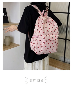 Pink corduroy backpack featuring red strawberry prints shown on a model in a room