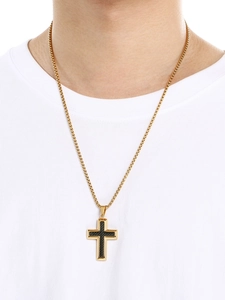 Gros plan d'un pendentif croix dorée avec incrustation noire et chaîne boîte sur un modèle