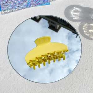 Creative shot of large yellow hair claw clip reflecting sky on a round mirror surface