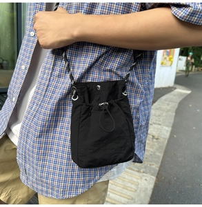 Close-up of black nylon drawstring crossbody bag worn by a model in outdoor setting