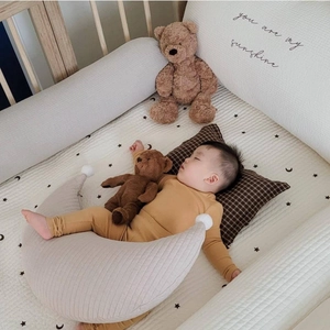 Cozy nursery setup with moon pillow, knitted cotton baby onesie and plush bear accessory