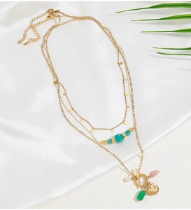 Dettaglio di una collana multistrato in ottone dorato con perline verdi e ciondolo a conchiglia