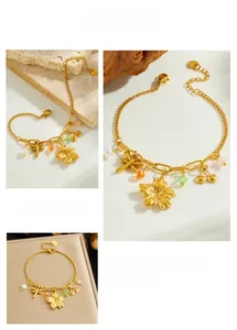Detailed close-up of gold cherry flower and dragonfly charms on a pearl stainless steel bracelet
