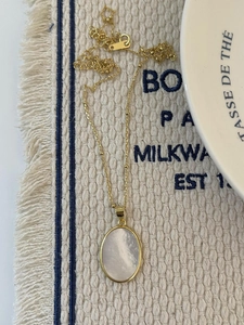 Detail of a gold oval shell pendant necklace on a textured beige woven mat