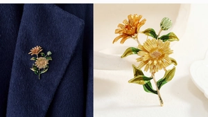 Detail of a daisy brooch with yellow enamel petals and green leaves on a blue blazer