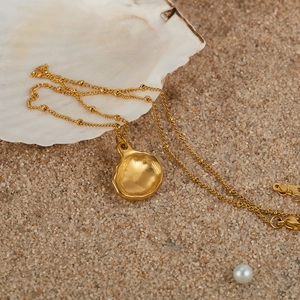 Artistic close-up of a gold shell necklace on beach sand with real shells and pearls
