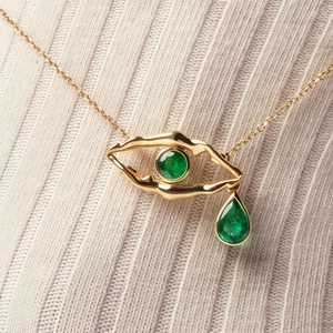Macro view of gold eye-shaped necklace with circular and teardrop emerald gemstones
