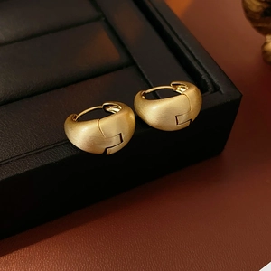 Detail view of matte gold brushed metal C-shaped hoop earrings on black leather display