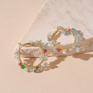 Détail des boucles d'oreilles créoles dorées avec pierres bleu clair et perles fines