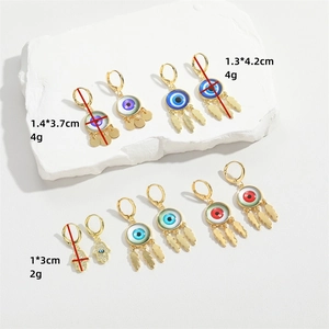 Golden Evil Eye and Hamsa Hand earrings displayed on white minimalist stone platforms