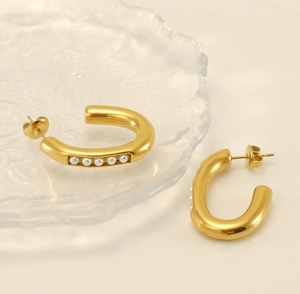 Macro detail of gold U-shaped hoop earrings featuring inlaid pearls on glass surface