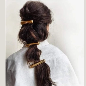 Close-up of three golden cylindrical hair clips styled on a low ponytail hair design