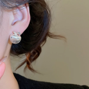 Macro view of silver apple-shaped stud earring with zircon inlay and brushed finish