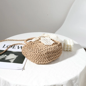 Beige woven straw handbag with lace ribbon bow on table for summer beach vacation