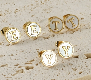 Macro view of gold stainless steel alphabet earrings with white shell inlay on stone