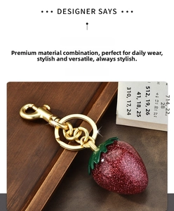 Detail of red glitter strawberry keychain with brass hardware and green leaf charm