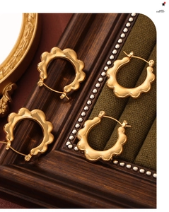 Macro detail of gold-plated sun-petal hoop earrings on a vintage green velvet display
