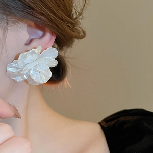 Detail of white 3D shell flower earrings with pearl accent worn by a model