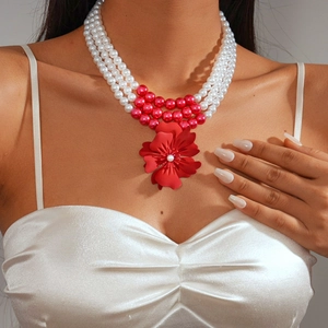 Close-up of triple-layer pearl necklace with red floral pendant on elegant white dress