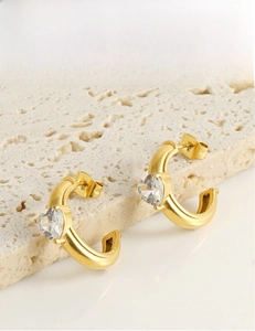 Détail de boucles d'oreilles créoles dorées en C avec zircon en forme de cœur