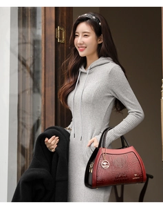 Detail of red and black crocodile embossed handbag with golden kangaroo pendant on model