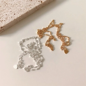 Detail of square link chains in gold and silver with small heart charms on stone tray