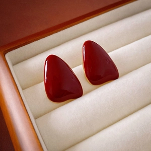 Macro shot of red enamel teardrop earrings with gold edges on a velvet jewelry box