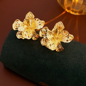 Macro shot of gold metal flower stud earrings with a textured hammered finish on velvet
