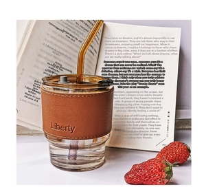 Detail view of glass coffee cup with brown leather sleeve and matching glass straw