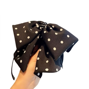 Handheld view of a large black and white polka dot bow hair claw with central bead details
