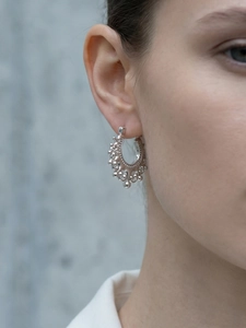 Macro detail of silver C-shaped hoop earrings with ethnic beadwork and carved textures