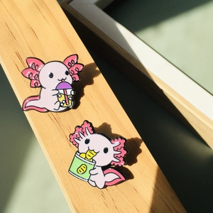 Lot de pins émaillés axolotl rose avec motifs bubble tea et collation sur fond bois