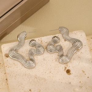 Macro detail of silver wavy streamlined metal earrings on a textured stone background