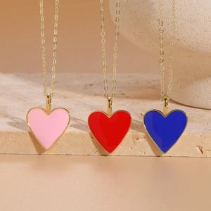 Three colorful enamel heart pendant necklaces in gold finish on a textured stone base
