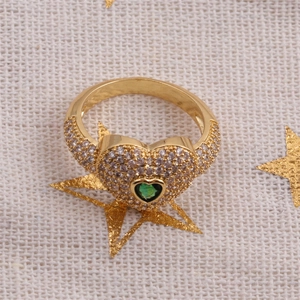 Détail de la bague coeur dorée avec pierre verte et cristaux pavés sur fond en lin beige