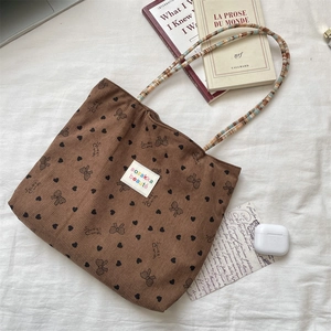 Detail of corduroy tote bag featuring bow heart prints and woven rope handles