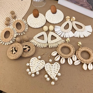 Vue à plat de boucles d'oreilles bohèmes en raphia avec paille coquillage et bois sur papier