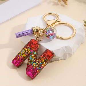 Close-up of resin letter N keychain with colorful sequins, purple tassel, and star charm