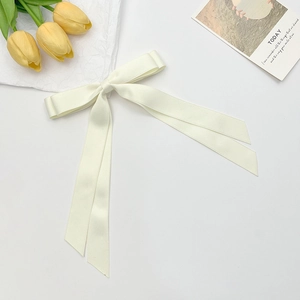 Close-up of cream double-layered satin bow hair clip with ribbons on aesthetic background