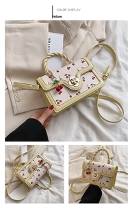 Detail view of cream crossbody bag with red cherry print and golden flower lock buckle