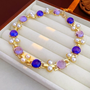 Gros plan d'un bracelet doré avec pierres violettes et perles dans un coffret bijoux