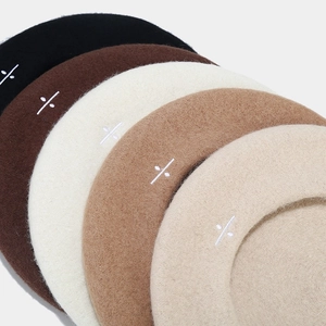 Detail of wool beret hats in multiple colors featuring minimalist leaf embroidery