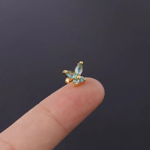 Close-up of a delicate gold butterfly ear stud with light blue zircon on a fingertip